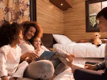 A family sat on a double bed in a cabin reading a book