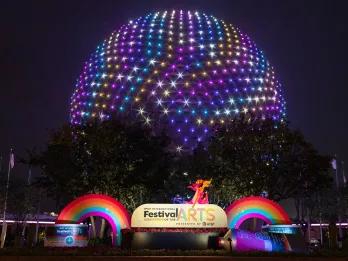 Spaceship Earth lit up in rainbow colours behind a sign reading Festival of the Arts