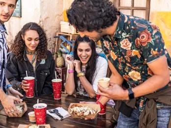 A group of 4 teenagers sat at a table eating food and drinking soft drinks from red cups 