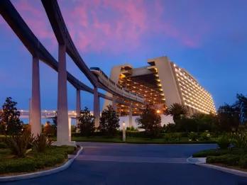 A modern A-frame shaped building with a monorail moving through it at dusk
