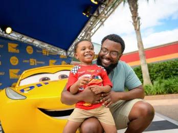 A dad and young son posing in front of one of the cars from Pixar's Cars