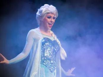 Elsa from Frozen standing on a stage with her arms out singing Let It Go