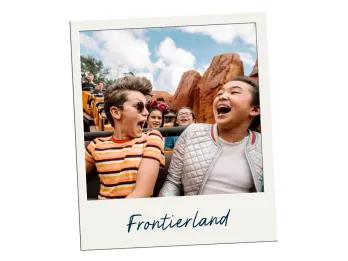 Two kids, one boy wearing glasses and one girl, are sat on a ride with wild west theming. In the background there are large orange rocks.