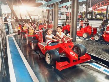 Small kids sat on rollercoaster car which is shaped like a red Ferrari Formula 1 car
