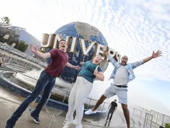 Three people jumping excitedly in front of the Universal Globe