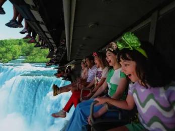 A row of people on a ride vehicle hanging a screen showing a waterfall