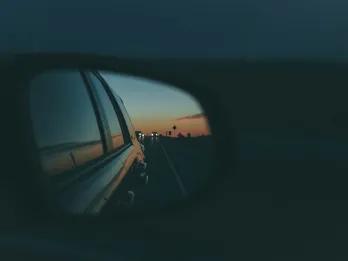 Dark night with car mirrors and in the mirror you can see the sun setting in the background and palm trees.