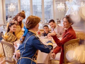 A family sat around a table in a restaurant being greeted by Belle and her prince