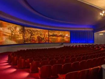 An empty theatre with rows of red seats in front of a large curved screen