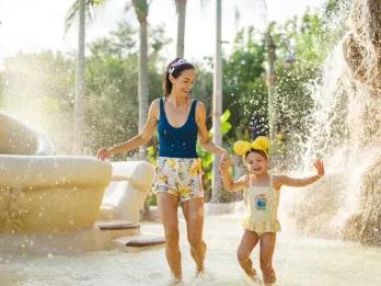 A mother and daughter splashing in a children's water play area