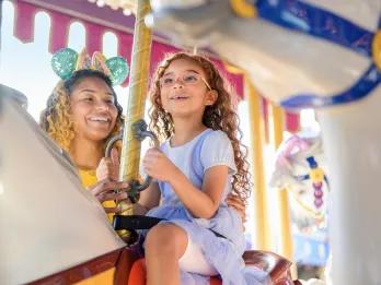 A girl and her mother riding a traditional carrousel 