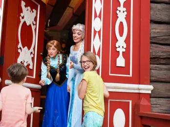Anna and Elsa from Frozen opening a door to greet two young children