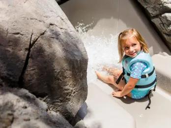 A young girl in a life vest about to go down a water slide