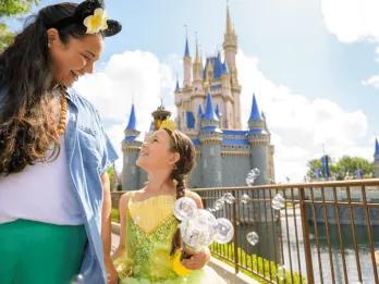 A mom and daughter in a princess dress walking in front of Cinderella Castle