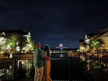A couple on a dock looking over a lake to a fireworks display
