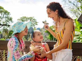 Mum with her two kids sharing a tub of ice cream in front of the statue of a shipwreck on a tall mountain.