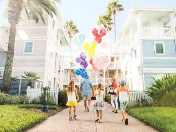A family walking towards colourful buildings holding Mickey Mouse-shaped balloons