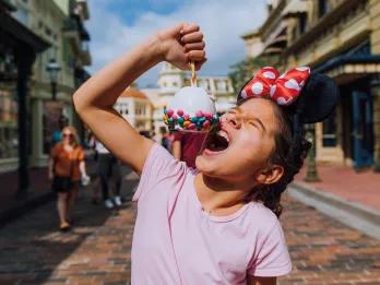 A young girl eating a candy apple wearing Minnie ears