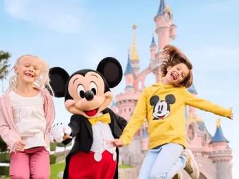 Zwei junge Mädchen springen mit Micky vor dem Schloss von Disneyland Paris
