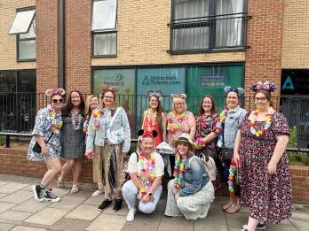 Group of women stood outside of an office building with windows with images of Mickey Mouse and the AttractionTickets logo on it. The women are dressed up for the summer party wearing florals and Mickey ears.