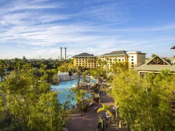 Large yellow resort with small river in front where the boats take guests to the park. In the background is a double drop tower and other rides in the parks.