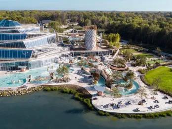 Huge water complex outside of a modern hotel building. There's a regular pool, long winding lazy river and other fun water activities.