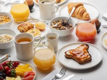 White table cloth set table with fruit plates, juices, cups of tea, toast with jam o it, croissants and many more delicious foods.