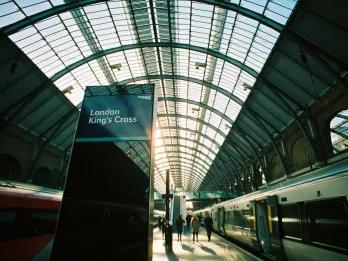 Large train station with a train waiting for passengers. There's a sign saying Kings Cross Station
