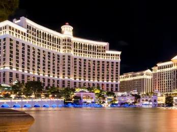 Tall white hotel with luxurious decor and a lake in front with fountains.