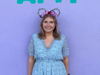 A girl stood in customised mickey ear headbands in front of a large purple wall and large writing above her head saying AMY.