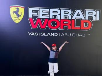 Girl stood in front of Ferrari World sign which has black background, red and white text and the Ferrari logo next to the name.