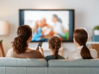 A woman, a teenager and a young girl watching TV from a sofa