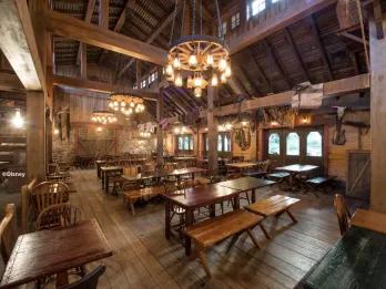 The rustic interior of Cowboy Cookout Barbecue at Disneyland Park, featuring exposed wooden beams, wagon wheel chandeliers, long wooden benches and Wild West décor in a spacious barn-style dining hall