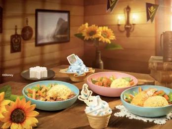 A spread of Nordic-inspired dishes at Nordic Crowns Tavern at Disney Adventure World, featuring hearty bowls of meat and vegetables, Frozen-themed desserts with Olaf decorations and a blue soft-serve sundae in a warm Arendelle-inspired setting