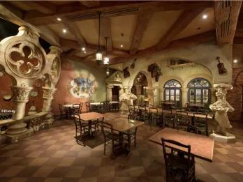 The charming Italian interior of Pizzeria Bella Notte at Disneyland Park, featuring rustic stone arches, wooden beamed ceilings, Lady and the Tramp inspired murals and chef statues in a warmly lit Fantasyland setting