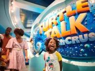 A child smiling with excitement in front of a sign reading Turtle Talk with Crush