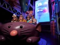 A family in a ride vehicle shaped like a large cartoon rat