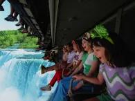 A row of people on a ride vehicle hanging a screen showing a waterfall