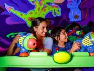 A mother and sun in a neon green ride vehicle using plastic laser blasters to shoot targets