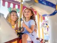 A girl and her mother riding a traditional carrousel 