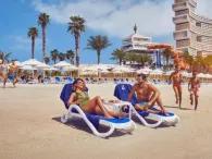 Two people relaxing on sunloungers while others run on the sandy Aquaventure Beach at Atlantis Dubai