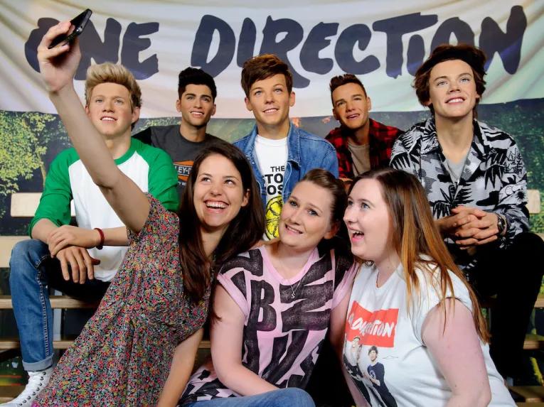 Girls having photo taken with One Direction at Madame Tussauds London