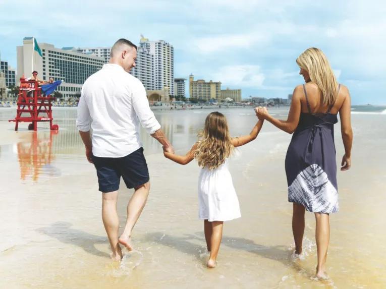 A family holding hands and walking along the shoreline on a Daytona Beach day trip from Orlando.