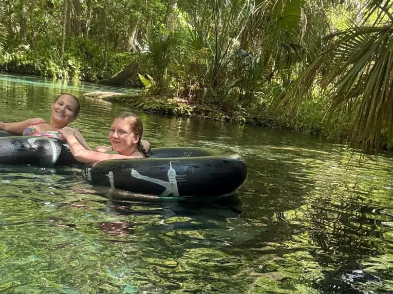 Two people smiling and floating on inner tubes down the clear waters of Rock Springs Run during a Rock Springs River Tubing and Apopka Wildlife Adventure tour.