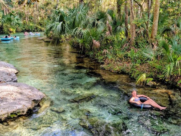 A young woman relaxing on a black inner tube in crystal-clear water on the Rock Springs River Tubing & Apopka Wildlife Adventure tour.