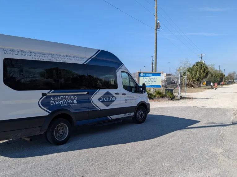 A Gray Line sightseeing tour van parked near the Lake Apopka North Shore entrance during a Rock Springs River Tubing & Apopka Wildlife Adventure tour.