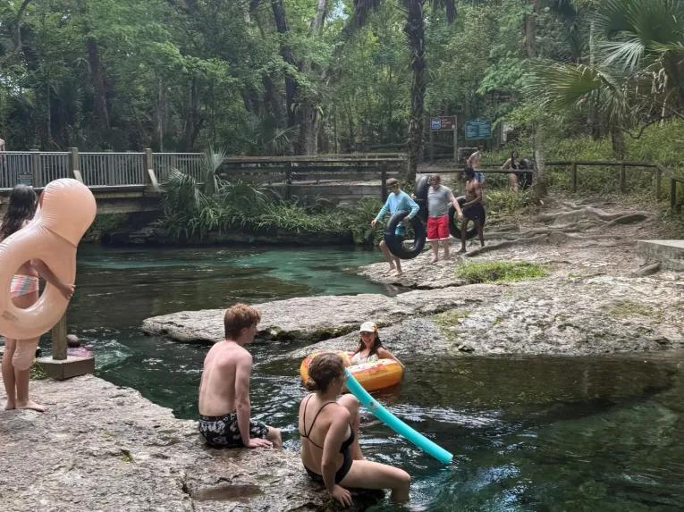 Visitors carrying inner tubes and relaxing by the rocky shoreline of a natural spring on the Rock Springs River Tubing & Apopka Wildlife Adventure tour.