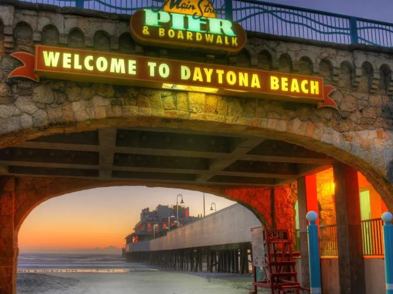 Welcome to Daytona Beach archway framing the pier at sunset.