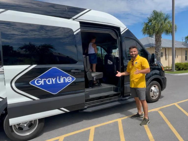 A Gray Line tour guide welcoming passengers into a comfortable black transit van.